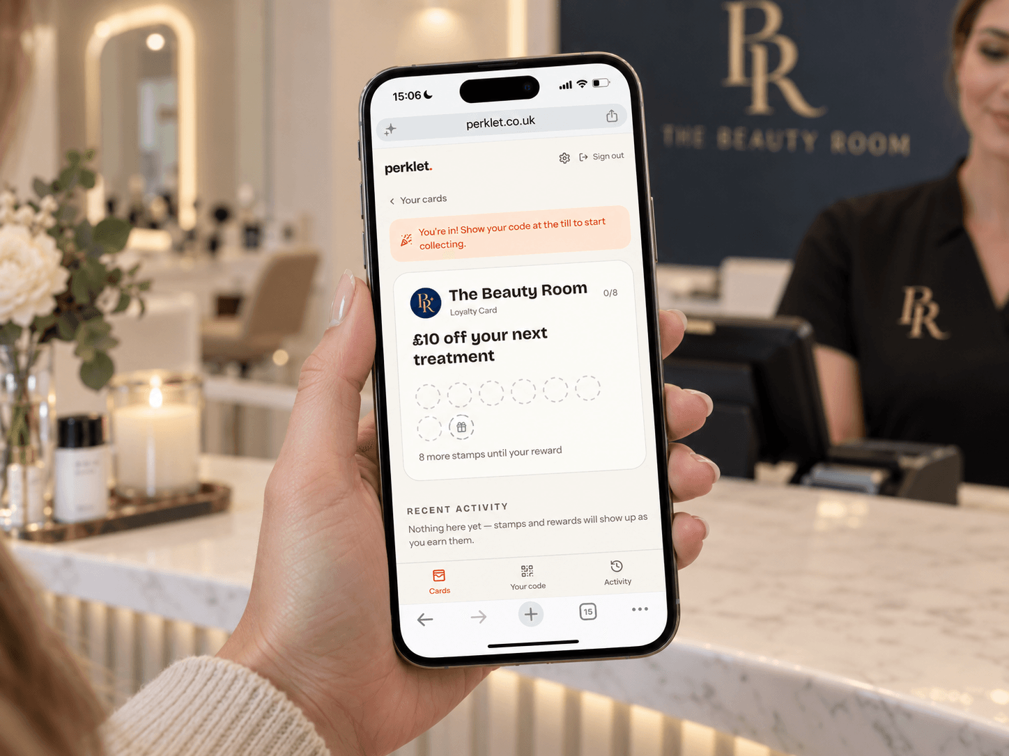 A customer holds up their phone showing The Beauty Room's digital loyalty card in the Perklet web app: £10 off your next treatment, 0 of 8 stamps collected.